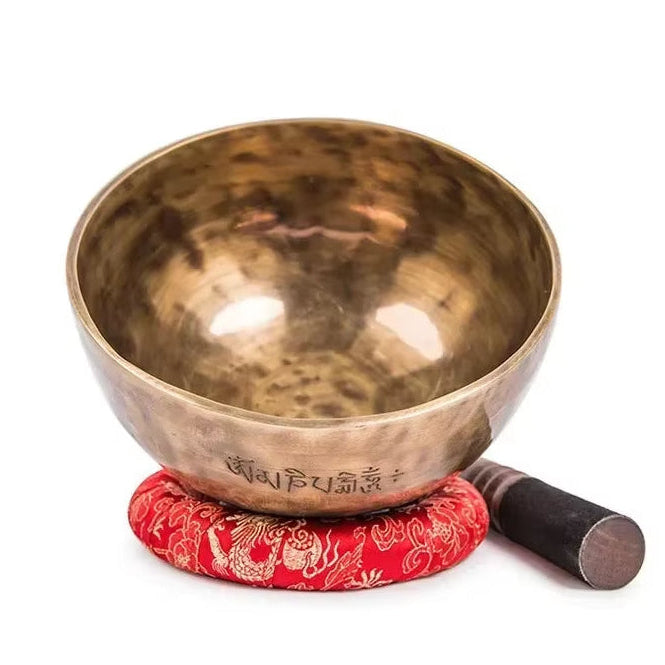 Hammered brass Tibetan Singing Bowl on a red cushion with a striker for meditation