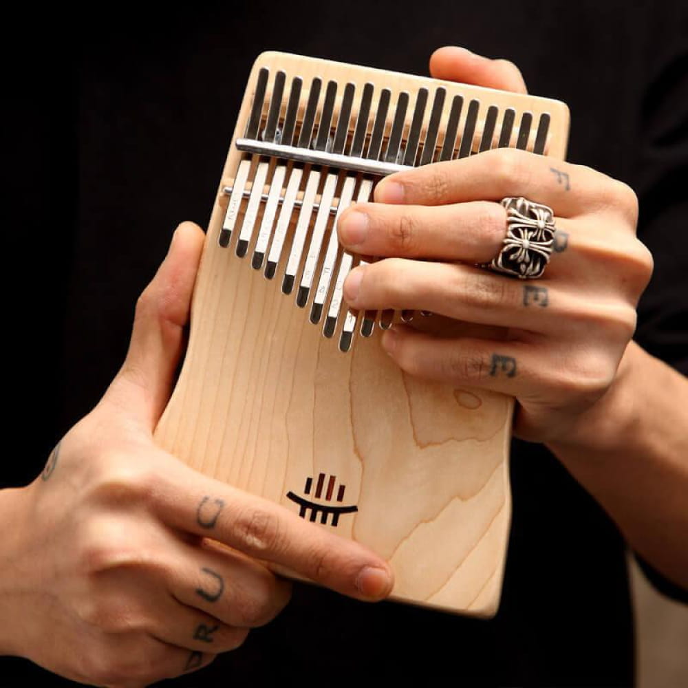 Wooden Kalimba with Metal Tines held by hands wearing decorative rings for meditation