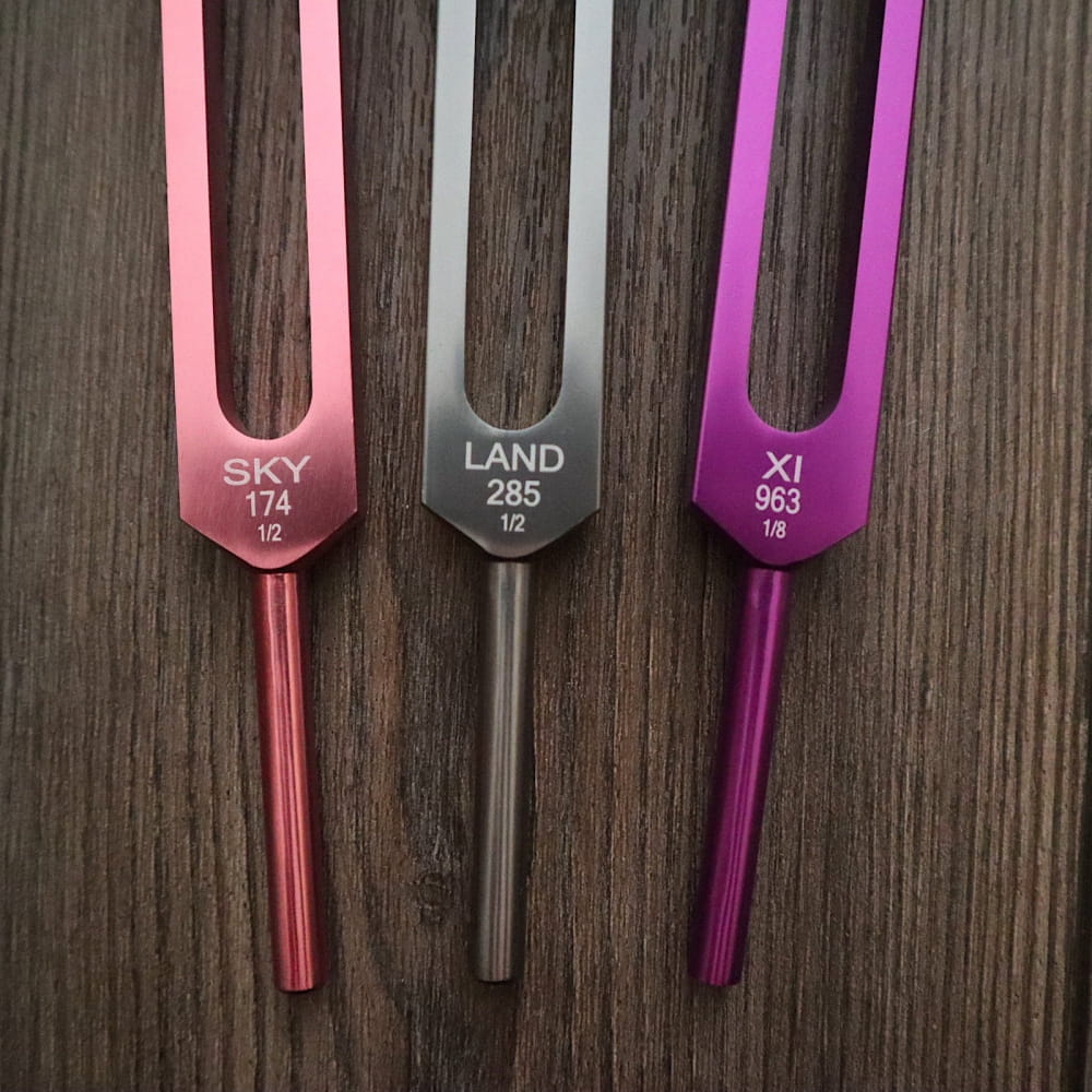 Three colorful tuning forks in pink, gray, and purple for Biofield Healing Therapy