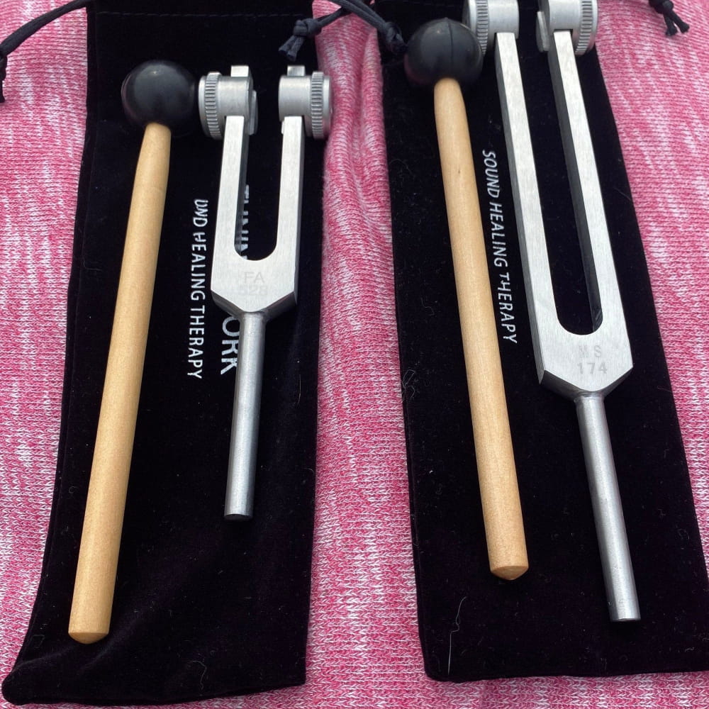 Two Healing Tuning Forks with Wooden Mallets on a Pink Surface