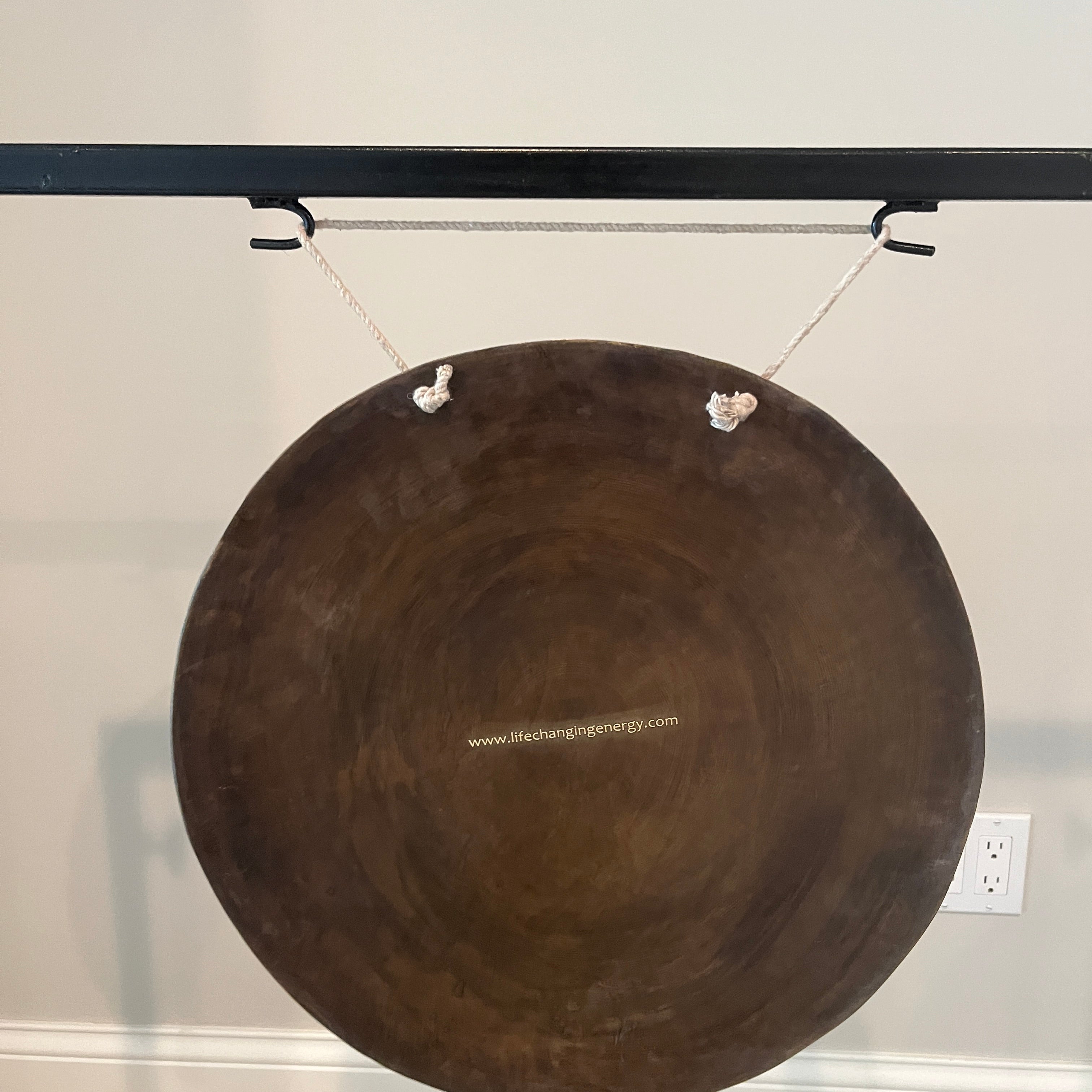 Circular brown metal gong with strings, part of 18’’ Bronze Wind Gong Instrument with Stand