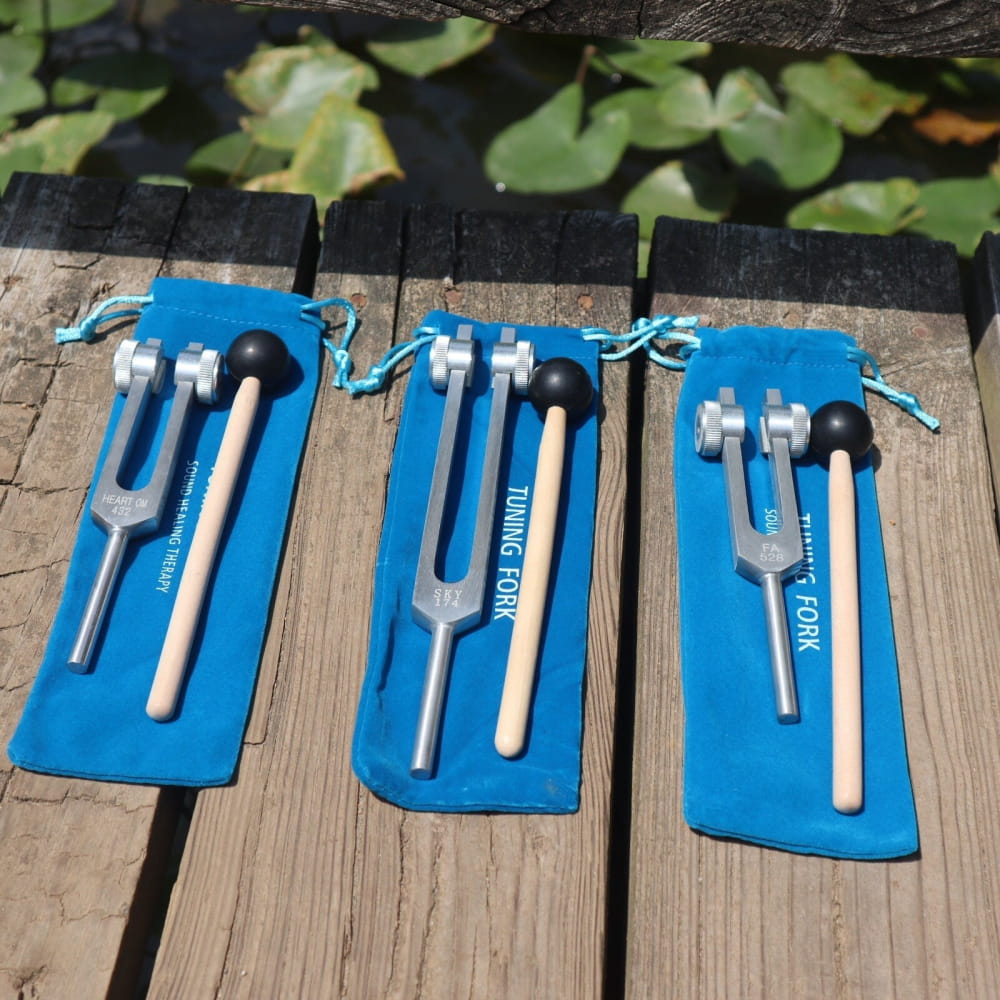 Three tuning forks with wooden mallets on blue fabric cases for healing frequencies