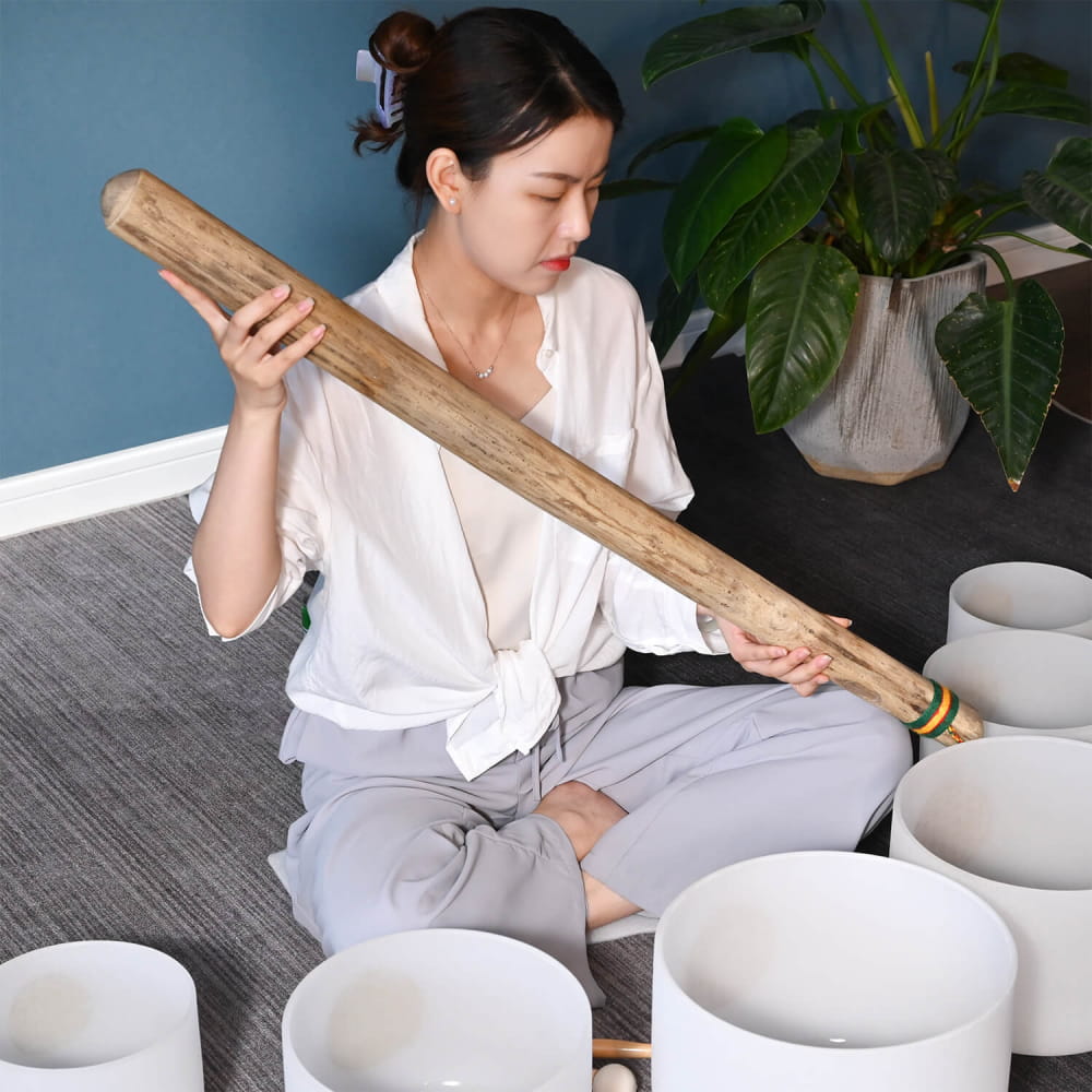 White ceramic singing bowls and a wooden mallet near 40 inch Handcrafted Rainstick
